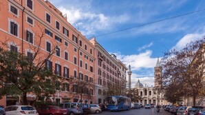 Una calle con coches aparcados y un autobús, edificios de arquitectura uniforme y un cielo despejado.