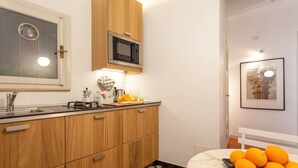 Una cocina con armarios de madera, un microondas, un lavabo y una encimera de mármol. Hay naranjas sobre la encimera y un cuadro en la pared.