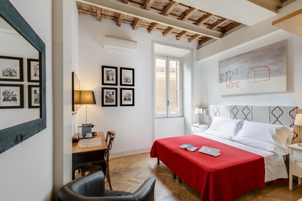 Une chambre avec un plafond en bois, un lit recouvert d’une couverture rouge, un bureau avec une lampe et des tableaux encadrés accrochés au mur.