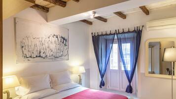 A bedroom with a wooden ceiling, a bed with a red bedspread, a nightstand with a lamp, a chair, and a table with a cup.