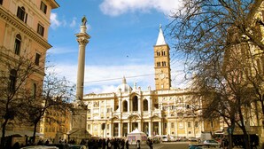 Un edificio histórico con una imponente torre de reloj y una columna central con una estatua.