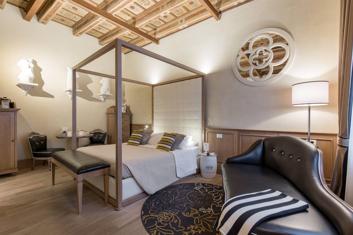 A four-poster bed with a canopy, a round rug with floral patterns, a leather sofa, and a wall-mounted round mirror.