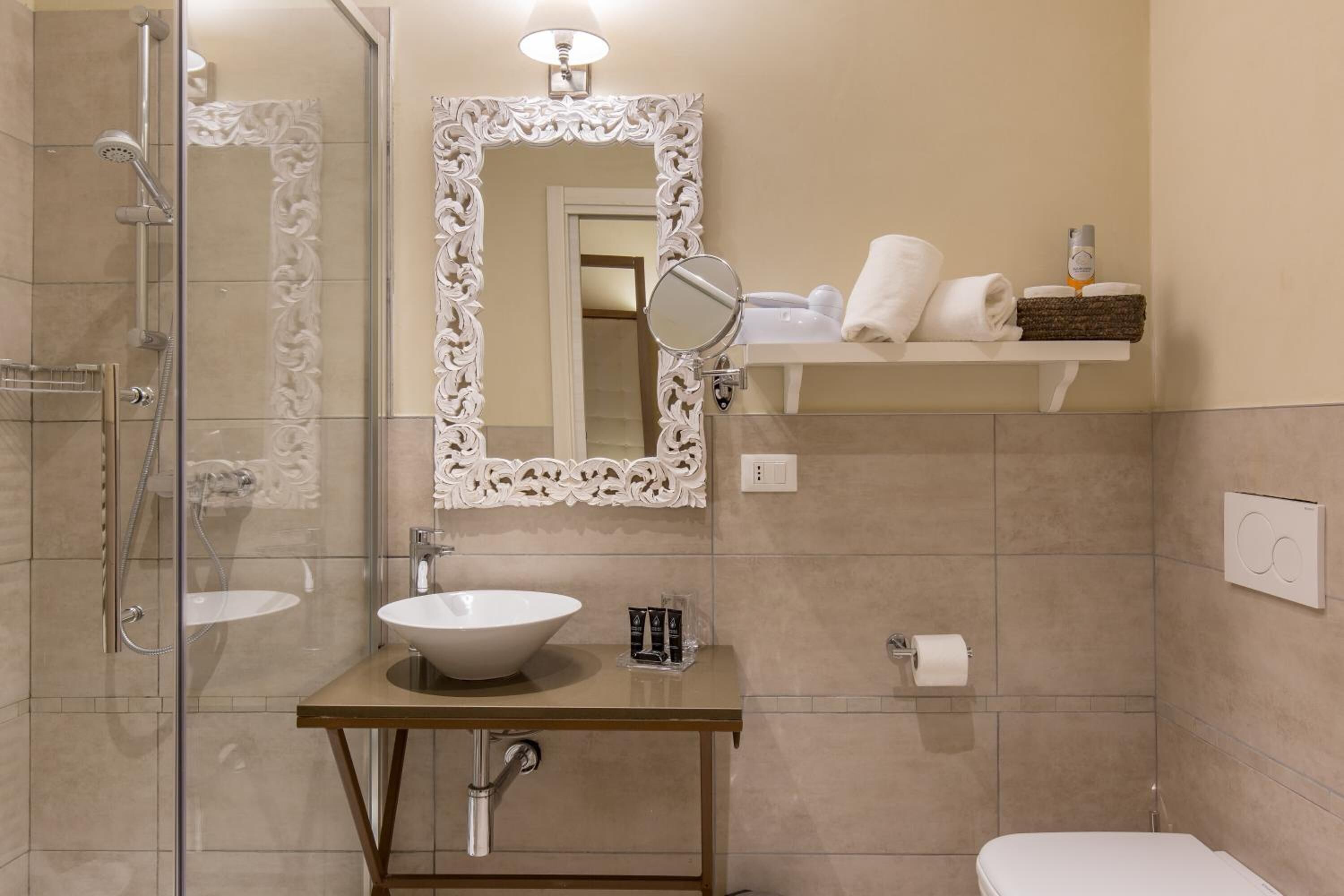 Une salle de bain avec une douche à parois de verre, un lavabo blanc, un miroir doté d’un cadre orné et un porte-serviettes avec des serviettes.