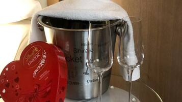 A champagne bucket with two glasses on a glass table, a red Lindor heart-shaped box, and a white towel on the bucket.