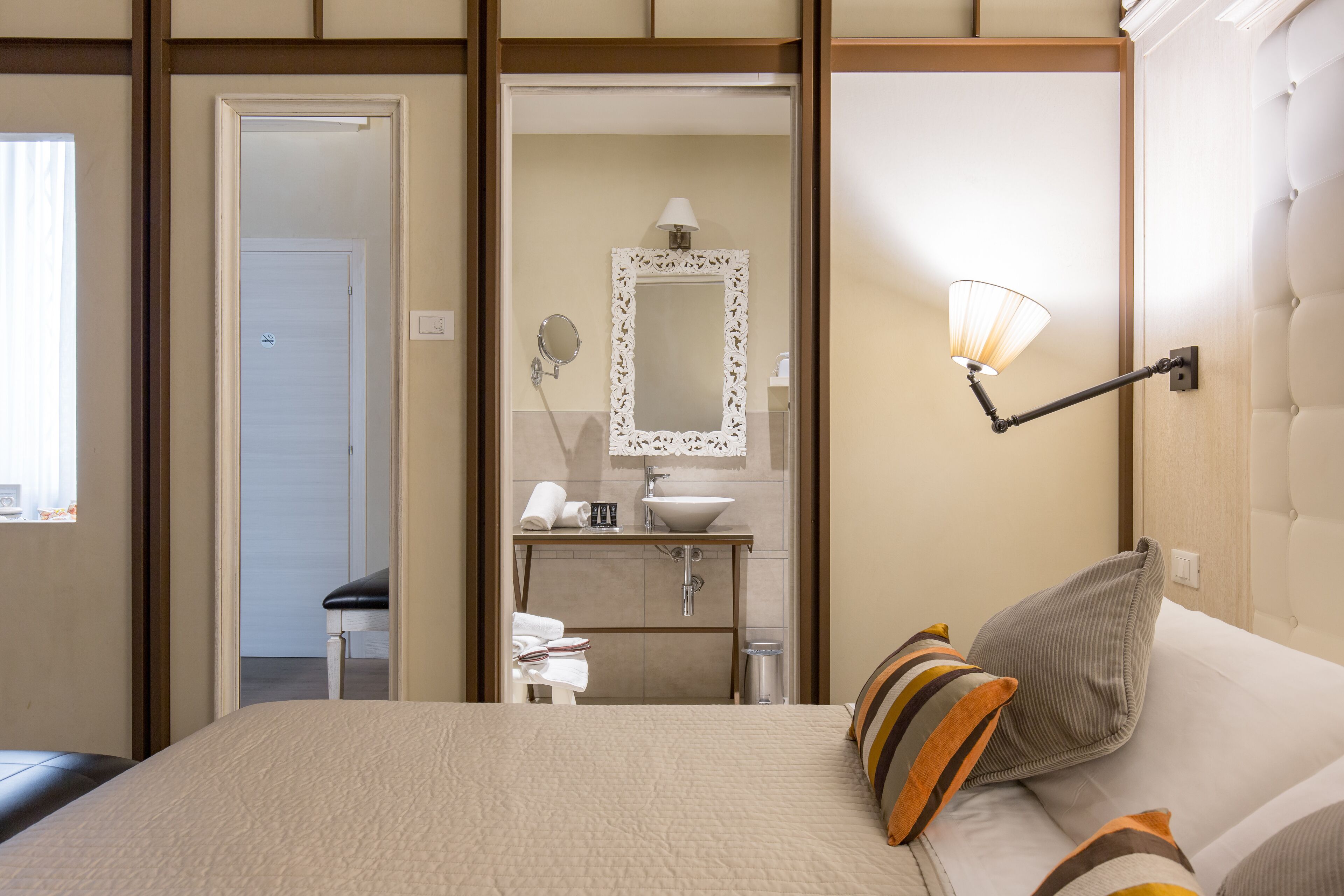 Habitación de hotel con cama, lámpara de noche, espejo, lavamanos y ventana.