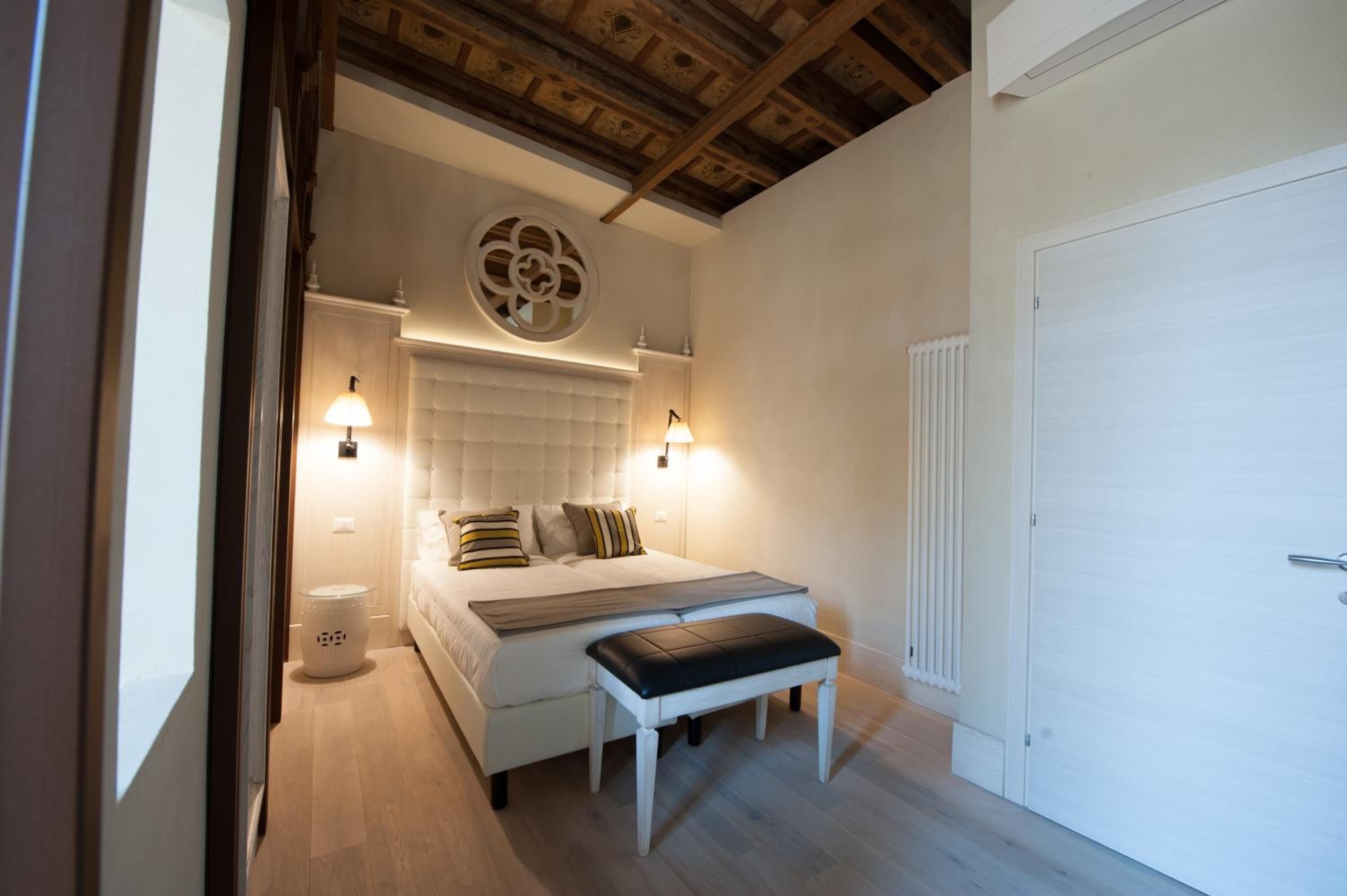 Un dormitorio con cama, lámparas de noche, un adorno redondo en la pared, un radiador blanco y una puerta blanca.