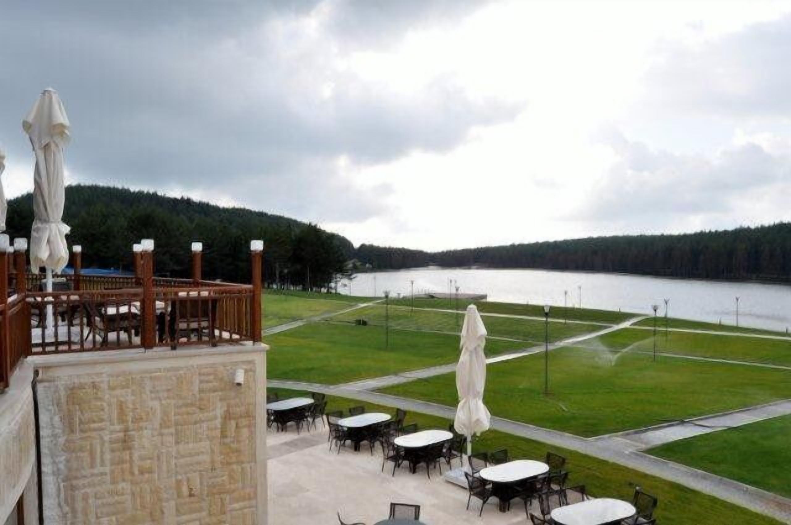 A terrace with outdoor seating overlooking a lake, surrounded by a forested area.