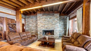A cozy living room with a stone fireplace, leather sofas, and a wooden staircase.