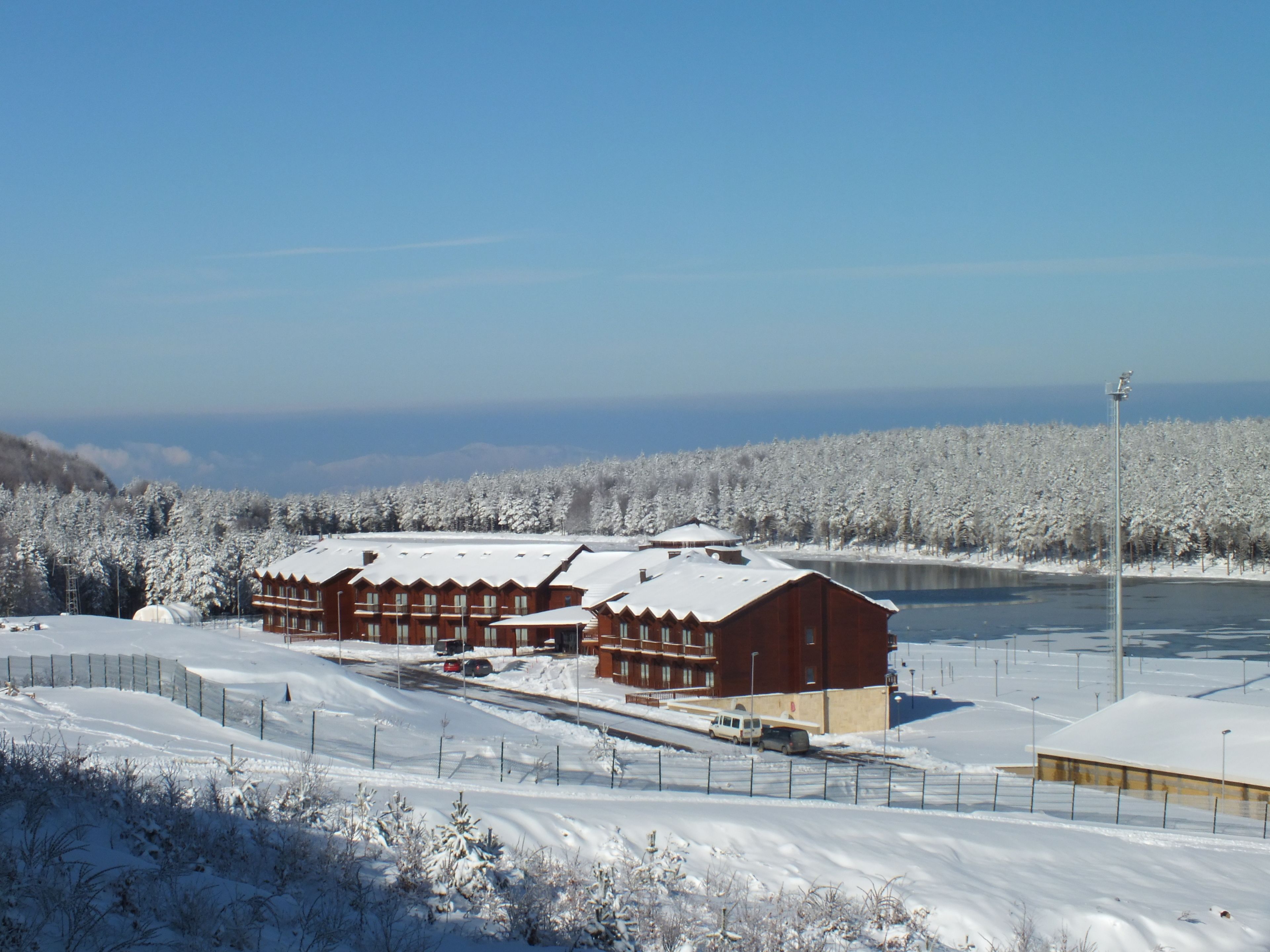 A snow-covered lodge with multiple buildings, a parking area, and a lake in the background.