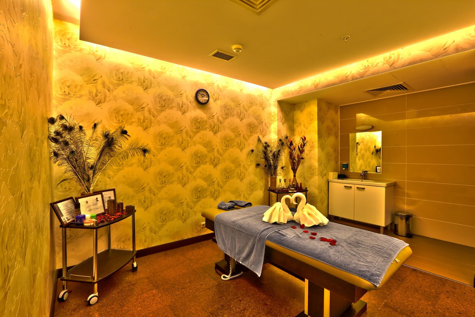 Uma sala de spa com mesa de massagem, toucador com espelho e plantas decorativas.