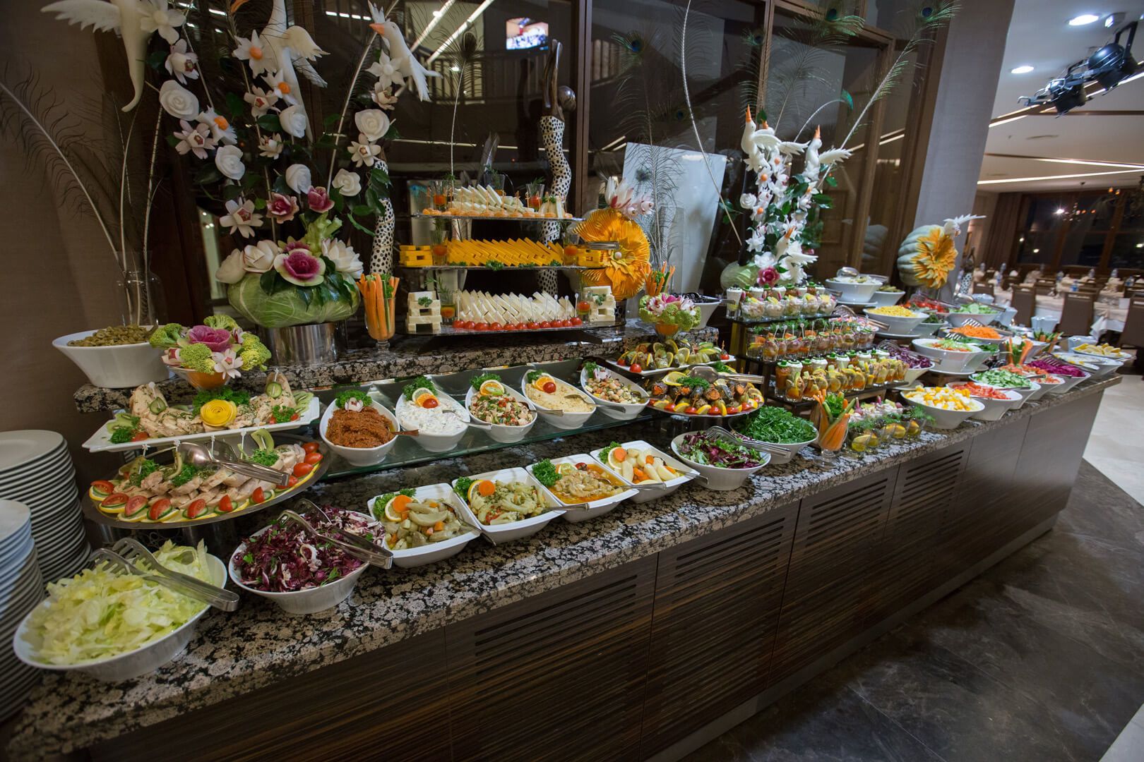 Un bufé con diversas opciones de comida y elementos decorativos como flores y plumas de pavo real.
