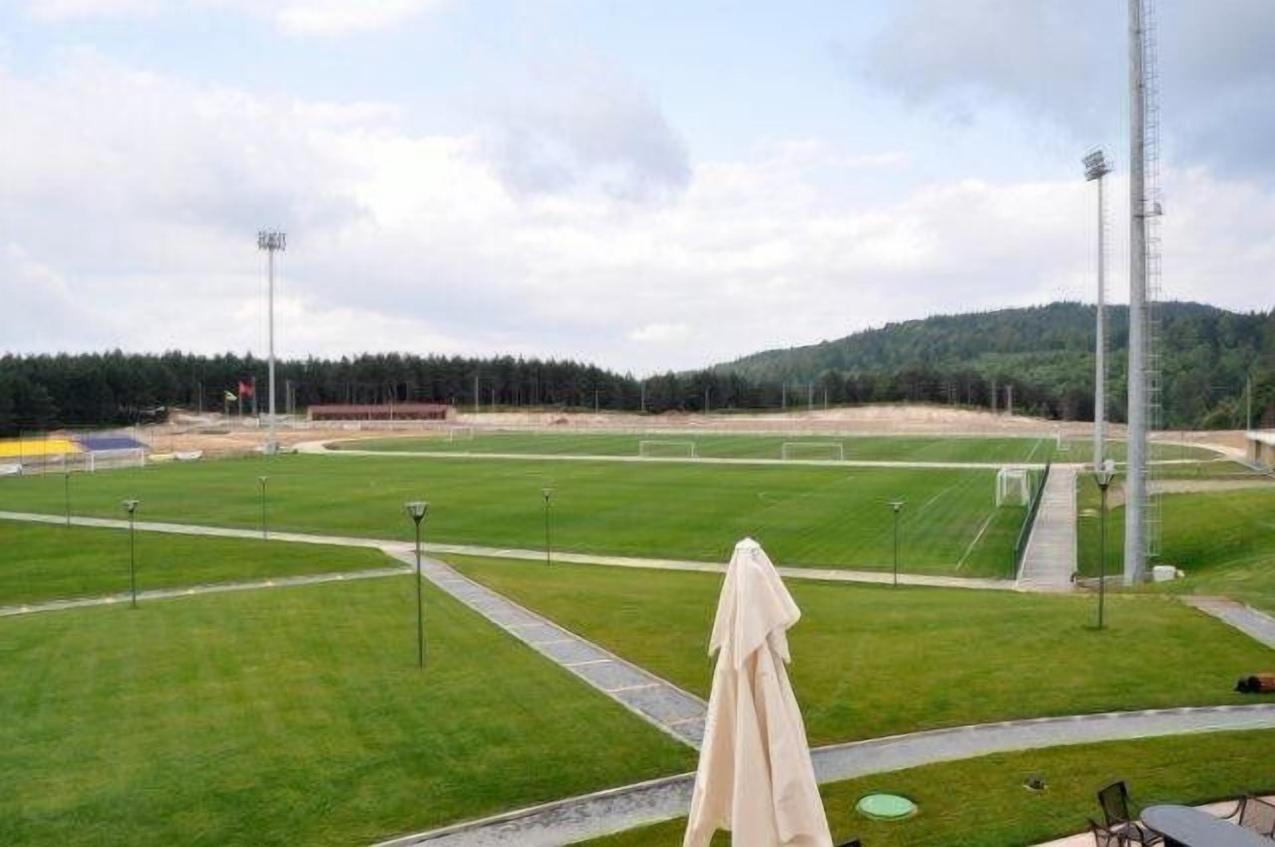 Um campo de futebol com postes de gol, iluminação e uma área de assentos coberta.