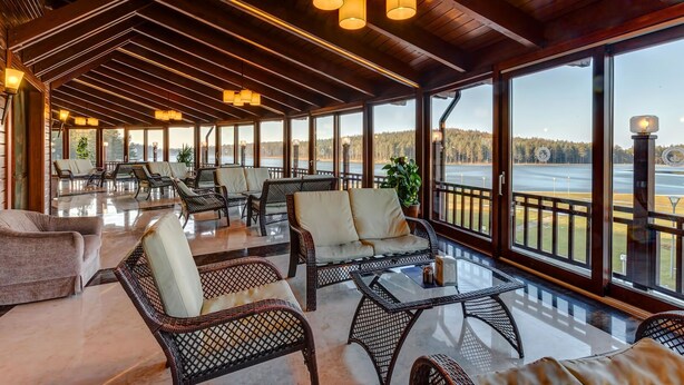 A spacious indoor area with wicker furniture, large windows, and a view of a body of water.