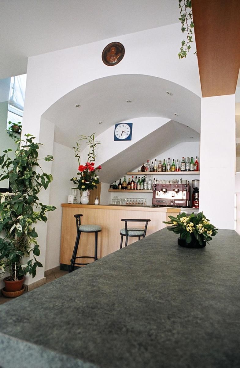 Zona de bar con techo curvo, un reloj y estantes con botellas. Hay dos sillas y una mesa con un florero.