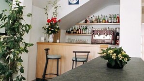 A bar area with a curved ceiling, a clock, and shelves with bottles. There are two chairs and a table with a vase of flowers.