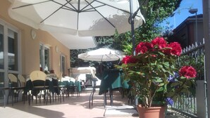 An outdoor patio area with tables and chairs, umbrellas, and potted plants.