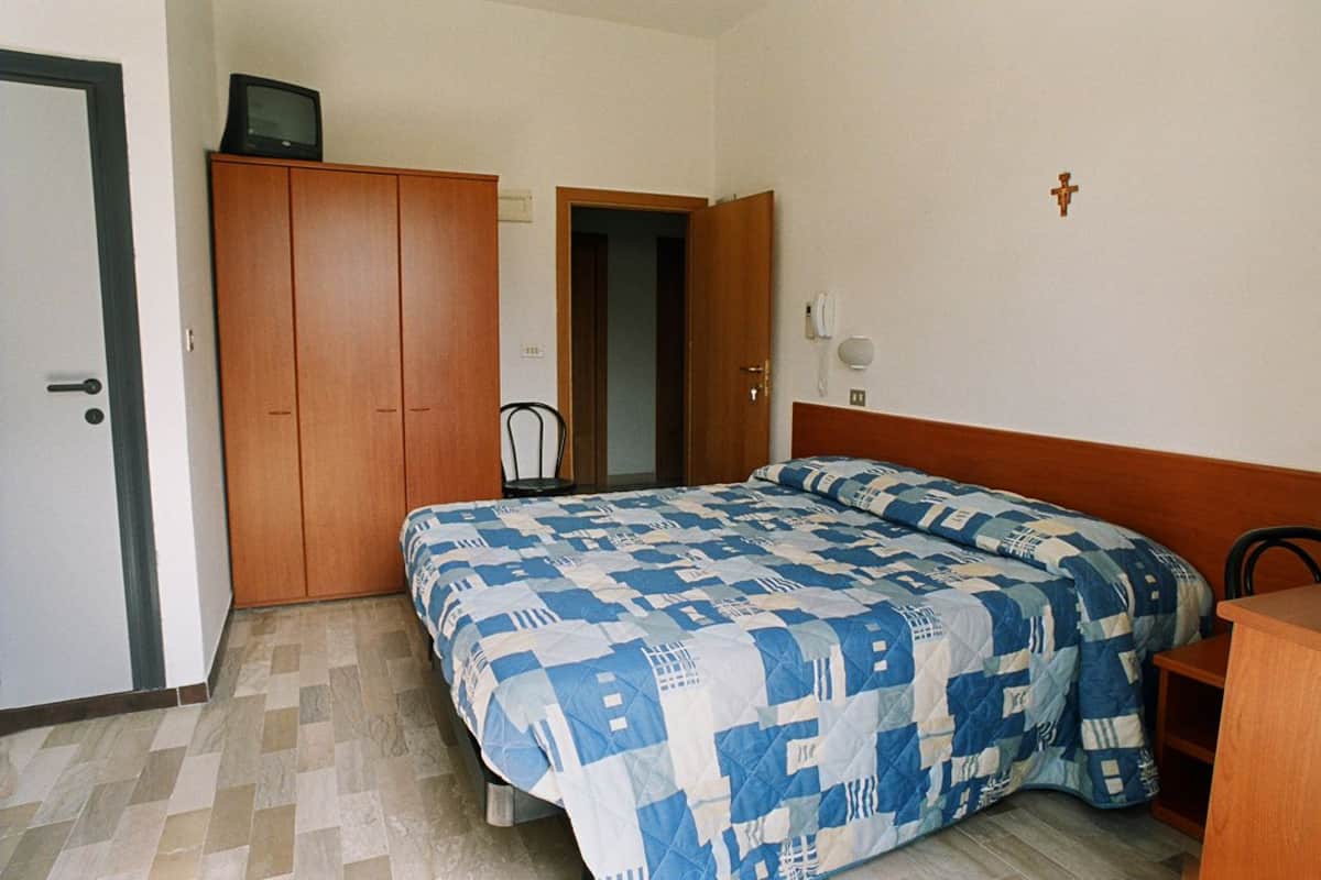 Quarto com cama, guarda-roupa, televisão em cima e uma cruz na parede.