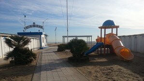 A pathway leading to a beach area with a playground, including a slide and a climbing structure.