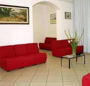 A living room with red sofas, a small table, and a painting on the wall. - Hotel Trinidad (Rimini)