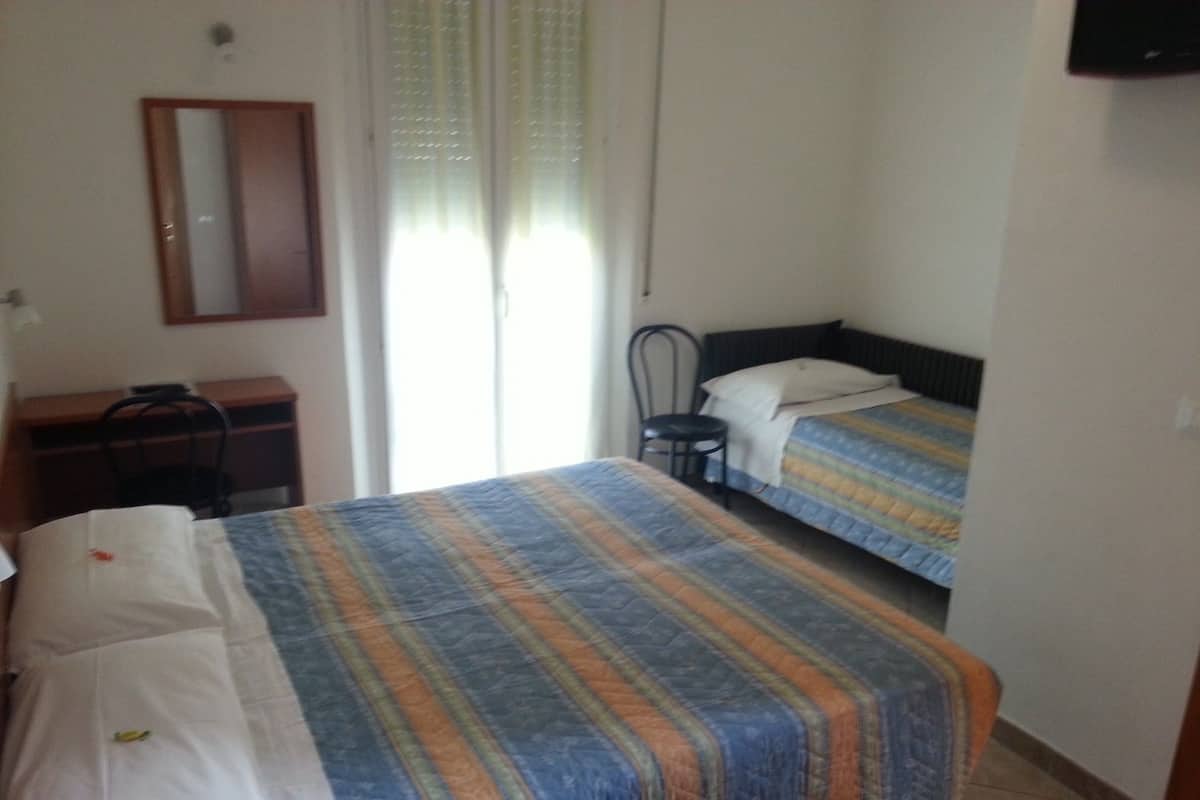 Quarto com duas camas, uma escrivaninha, uma cadeira e um espelho na parede.