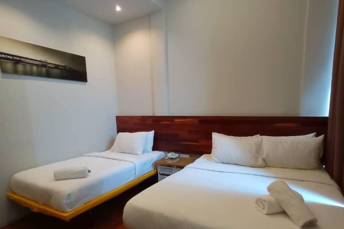 A hotel room with two single beds, a wooden headboard, a nightstand, and a ceiling light.