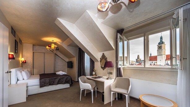 A hotel room with a bed, desk, two chairs, a small table, a window with a city view, and a chandelier. - Residence Mysterius Old Town  (Prague)