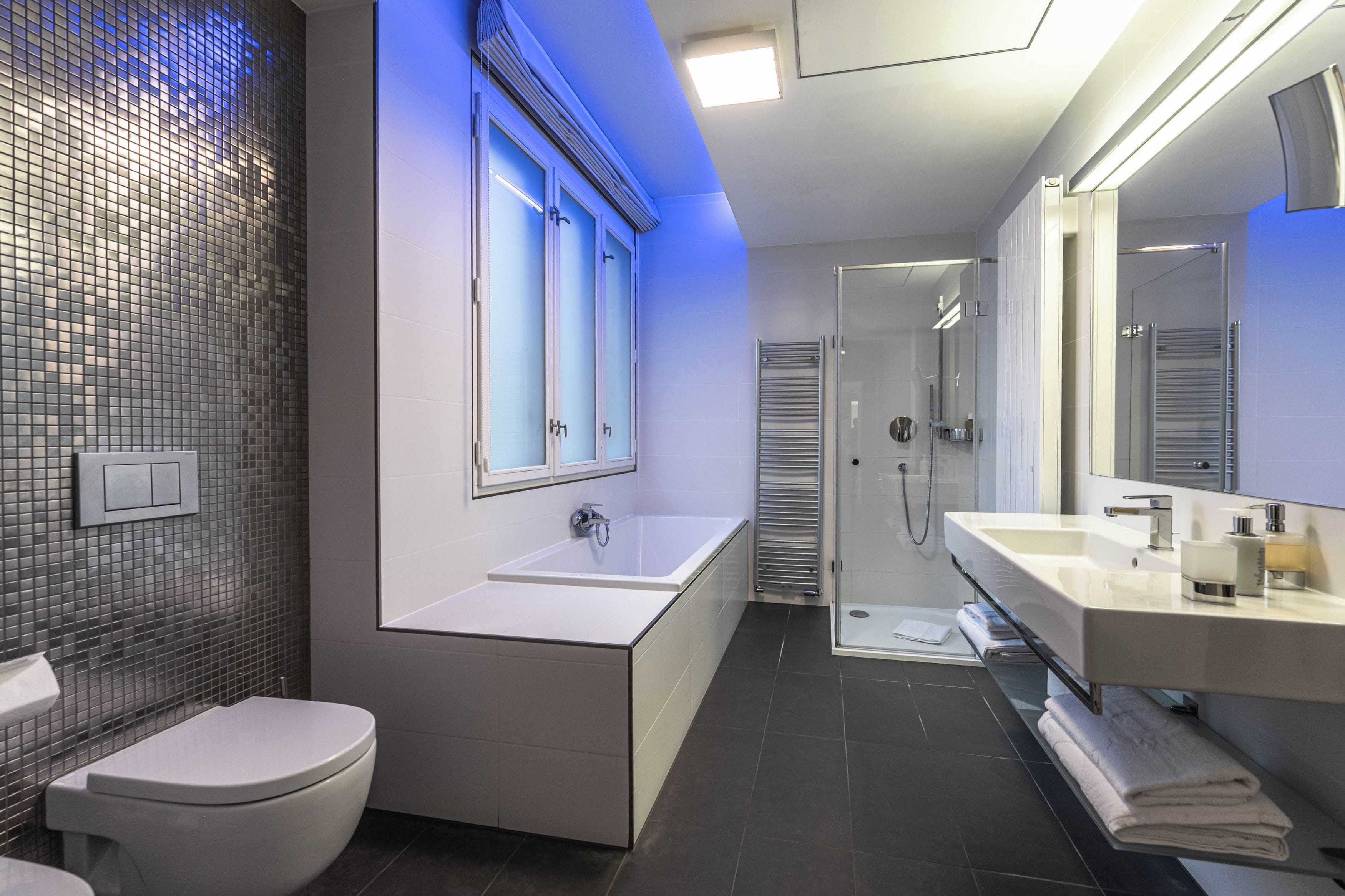 A modern bathroom with a toilet, a bathtub, a shower, and a vanity with a mirror.