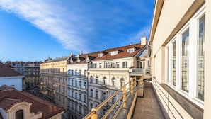 Un balcón con barandilla que da a una hilera de edificios históricos de diversos estilos arquitectónicos y un cielo azul despejado.