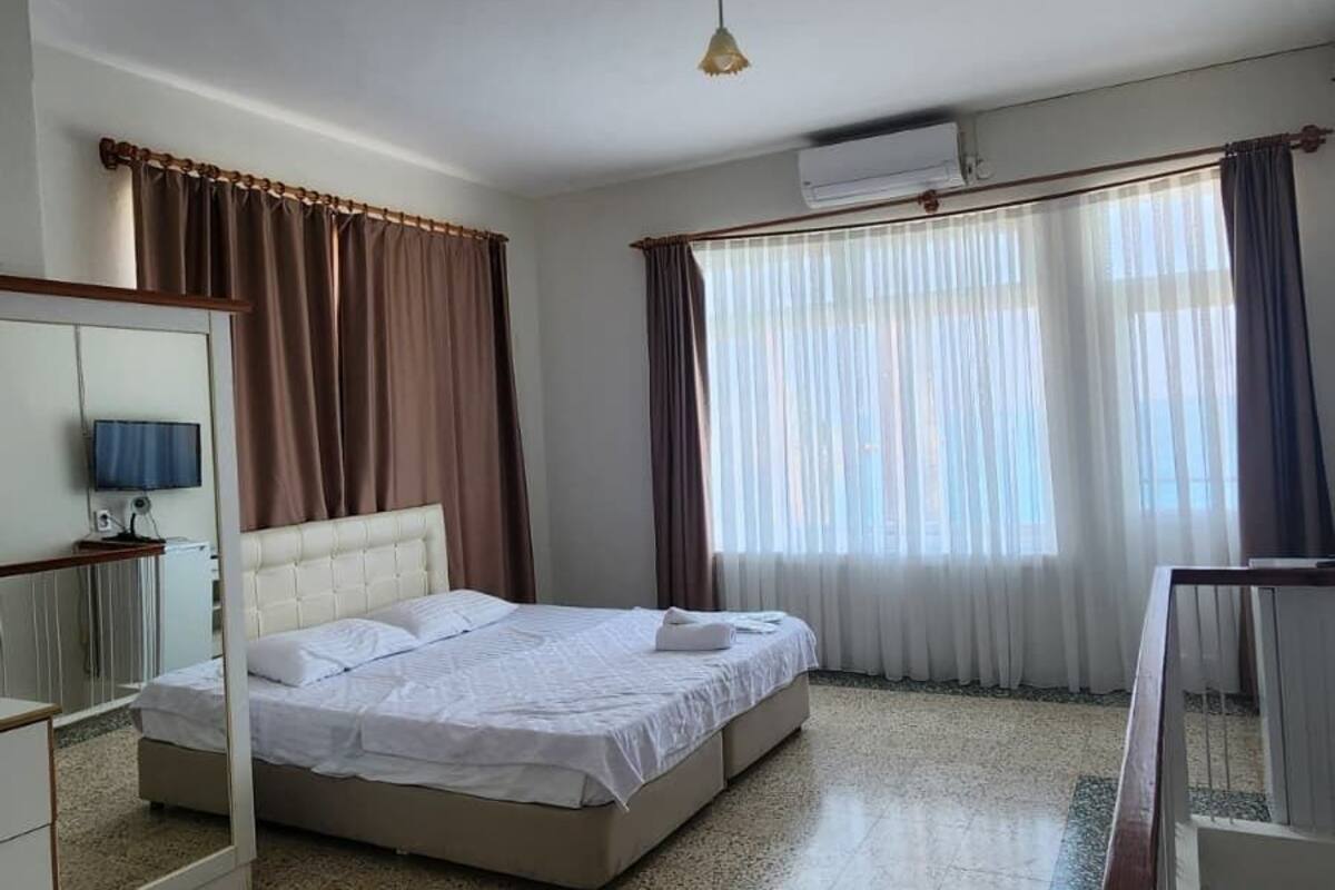 A hotel room with a bed, a desk, a chair, a TV, and an air conditioning unit.