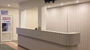 A reception desk with a sign for the swimming pool and a reception area with a white wall and ceiling lights. - Lades Hotel (Silifke)
