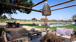 A patio area with outdoor furniture, a wooden table with drinks, a large tree stump, and a pool in the background. - Casa do Governador (Évora)