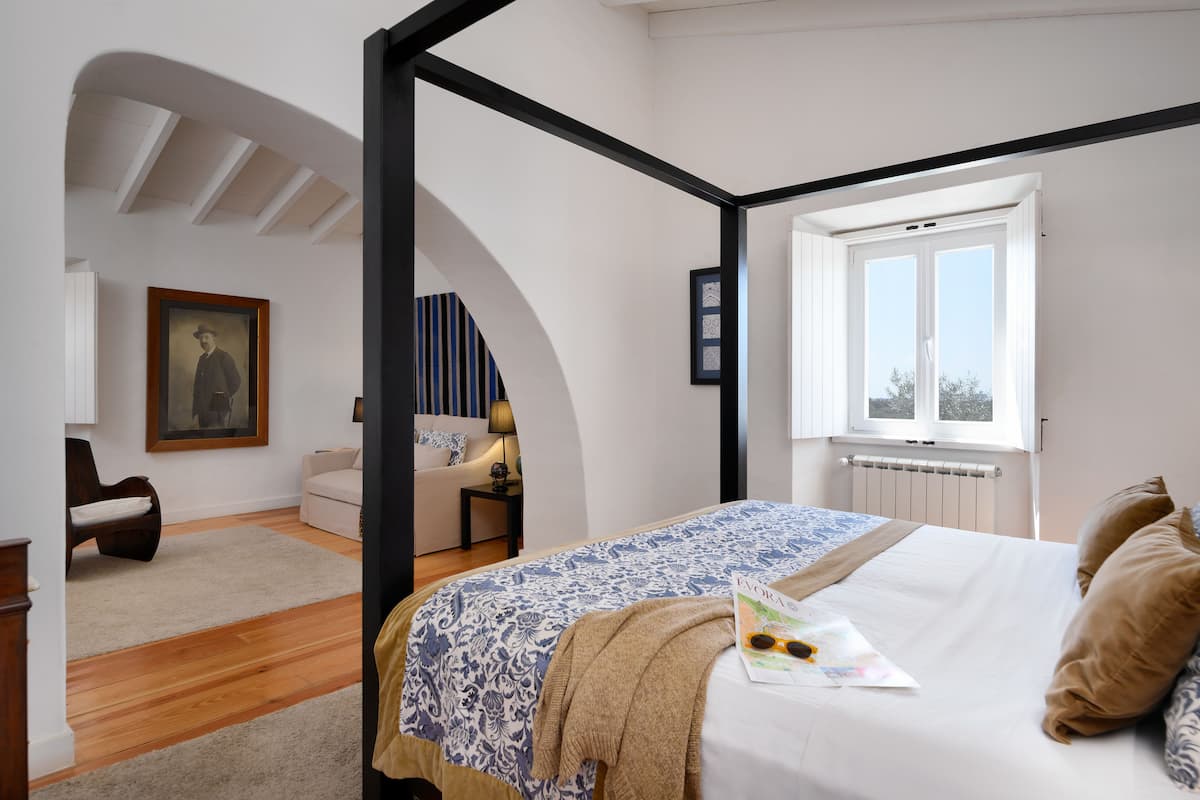 A bedroom with a bed, a window, a framed picture, and a chair.