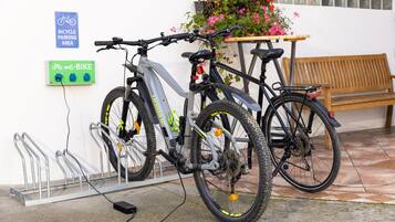 A bicycle parked at an e-bike station, a wooden bench, and a flower planter.