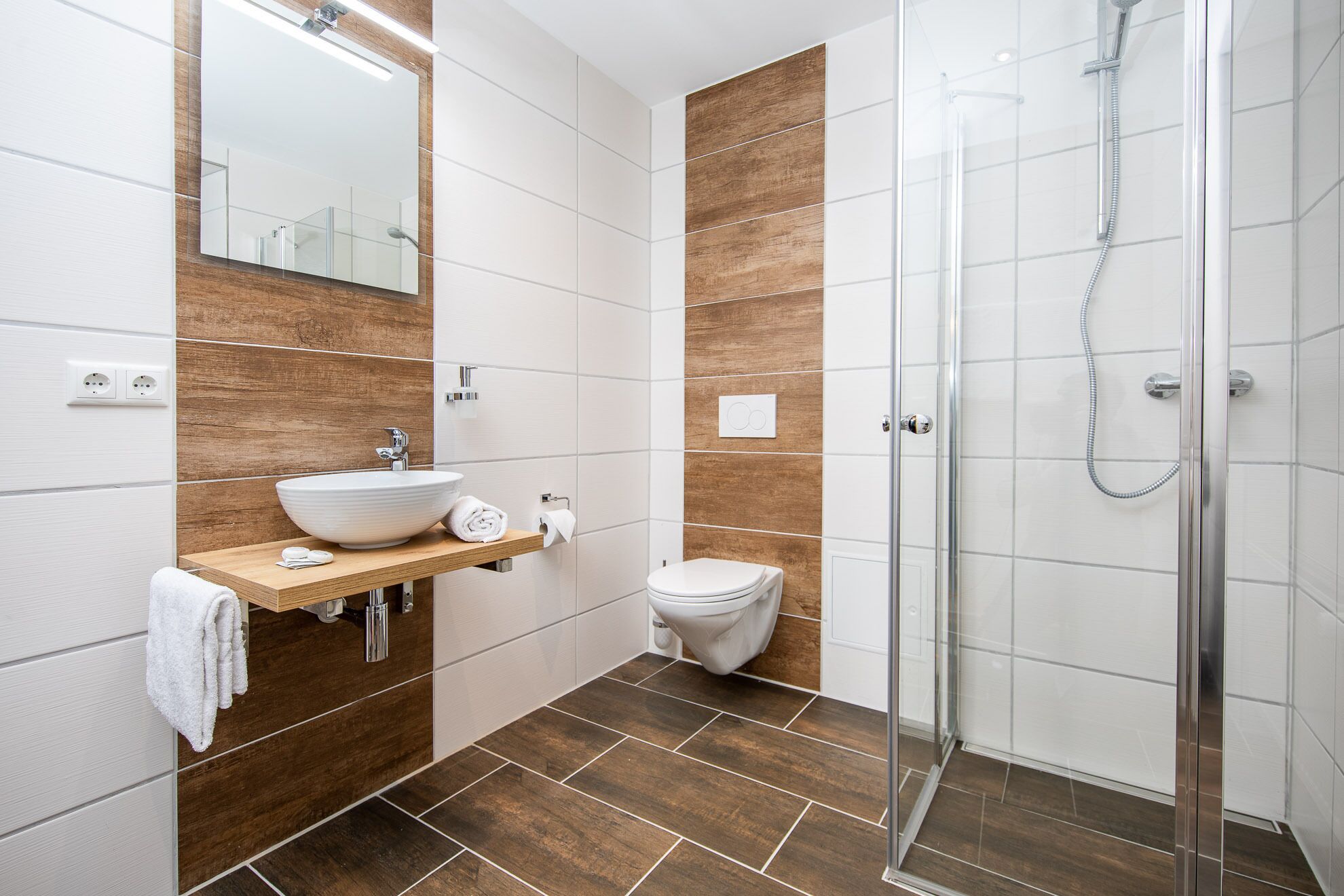 A modern bathroom with a glass shower enclosure, a white sink with a wooden vanity, and a toilet.