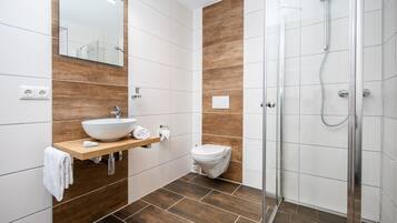 A modern bathroom with a glass shower enclosure, a white sink with a wooden vanity, and a toilet.