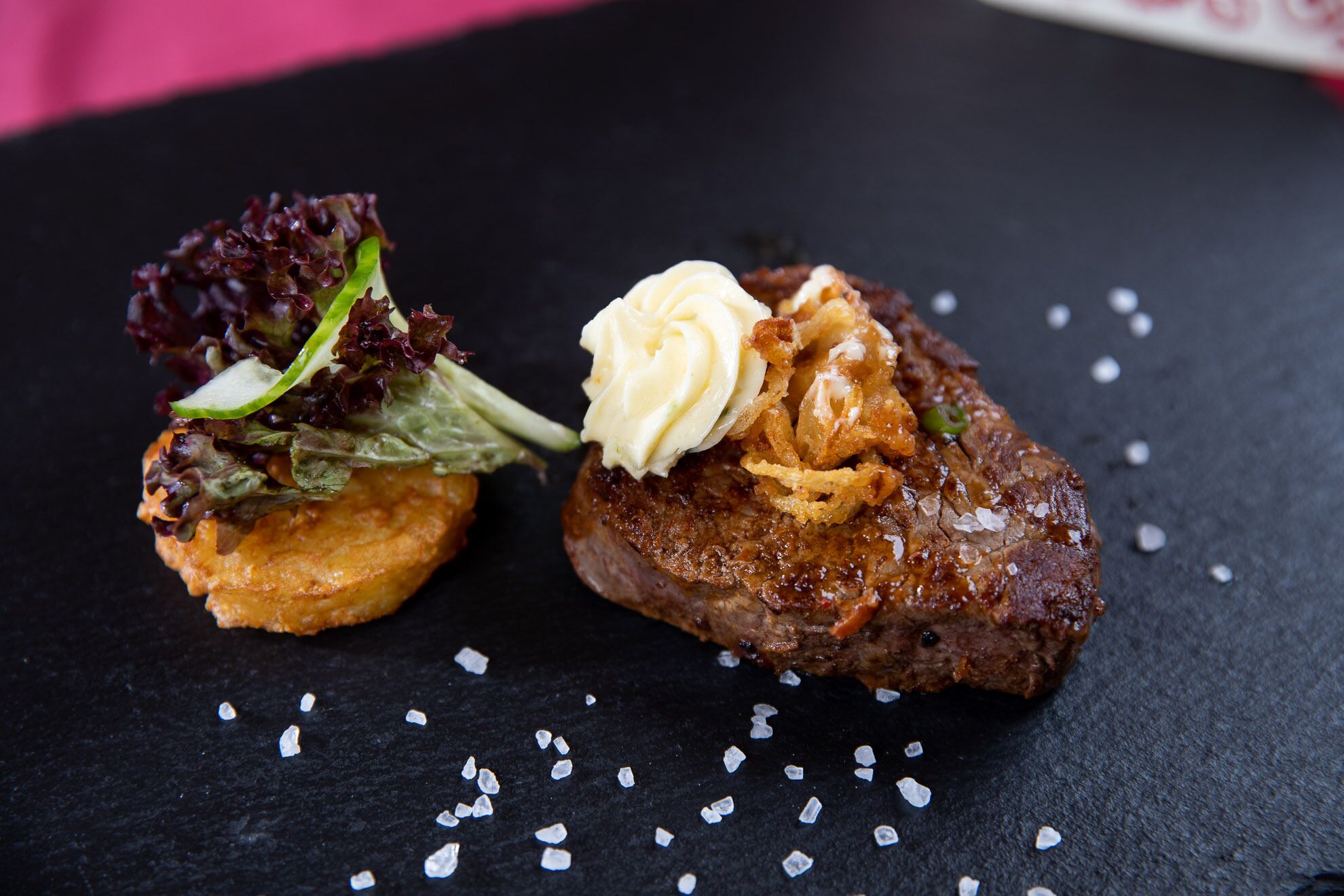 A steak with a creamy sauce and fried onions, accompanied by a side of greens and potato.