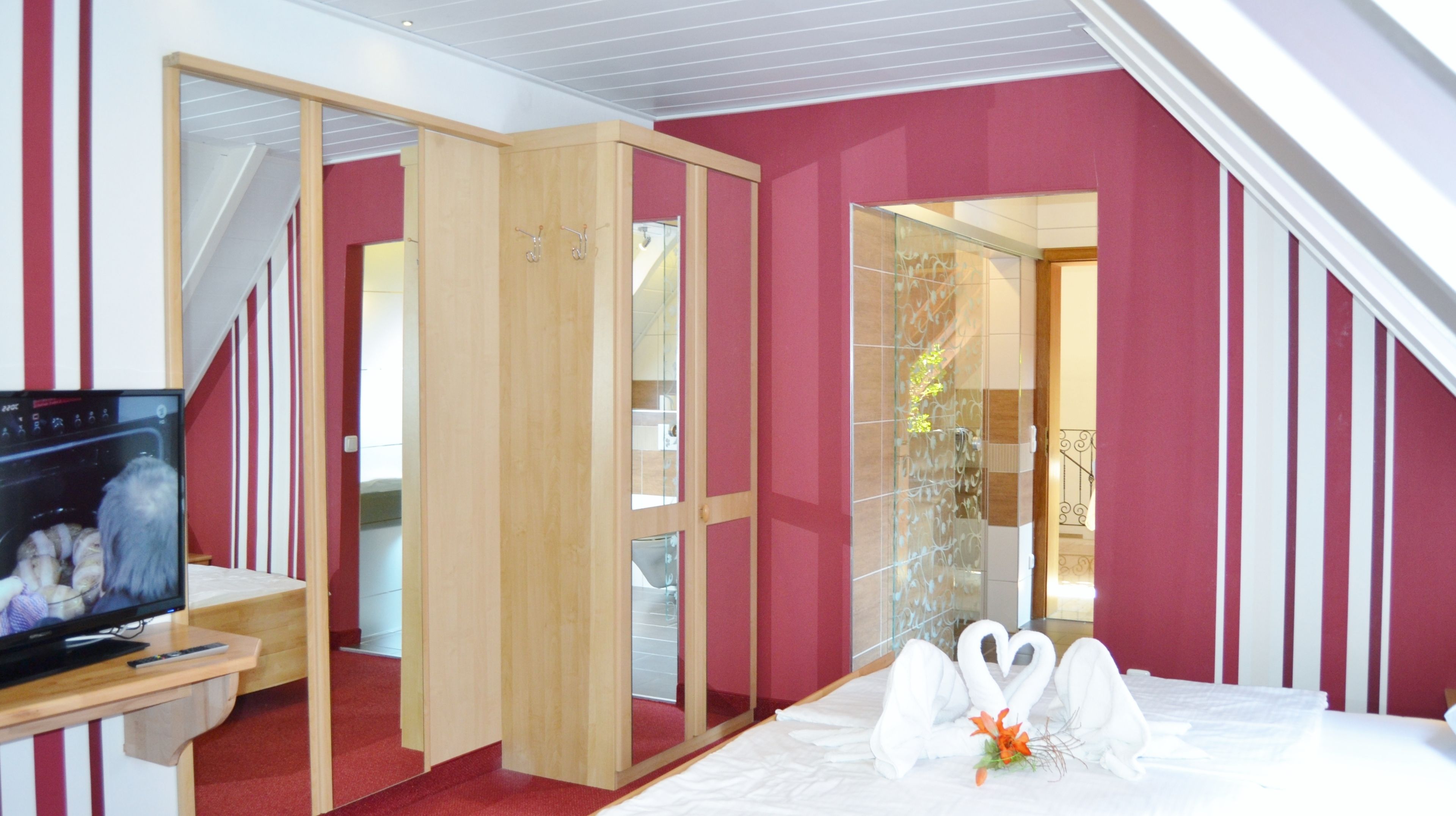 Une chambre d’hôtel équipée d’une télévision, d’une armoire en bois, d’un lit avec deux oreillers en forme de cygne et d’un mur à rayures rouges et blanches.