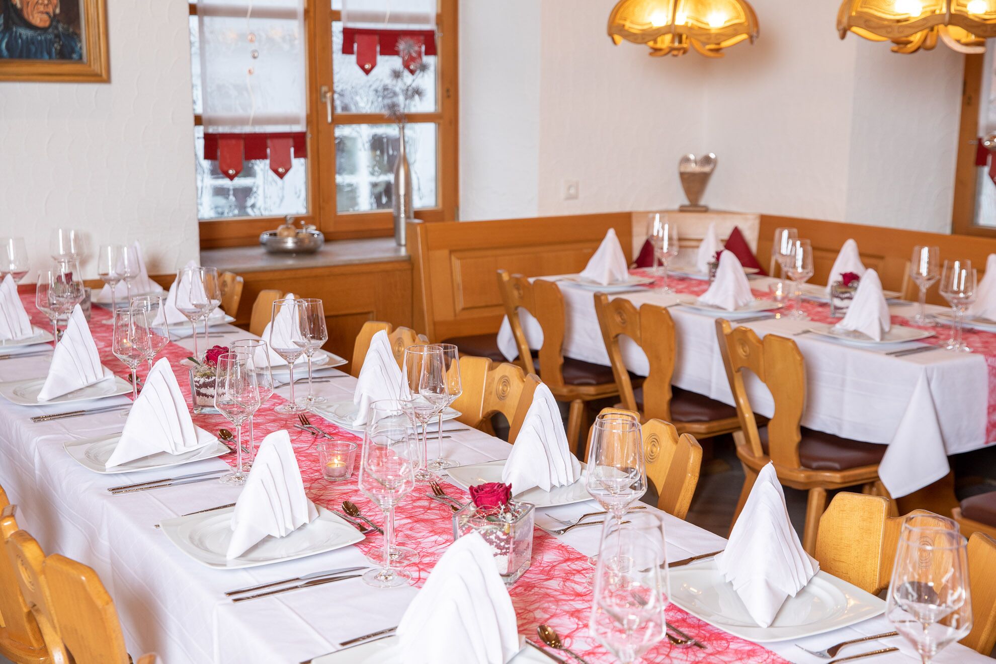 A restaurant with multiple tables set for dining, featuring white tablecloths and neatly arranged silverware.