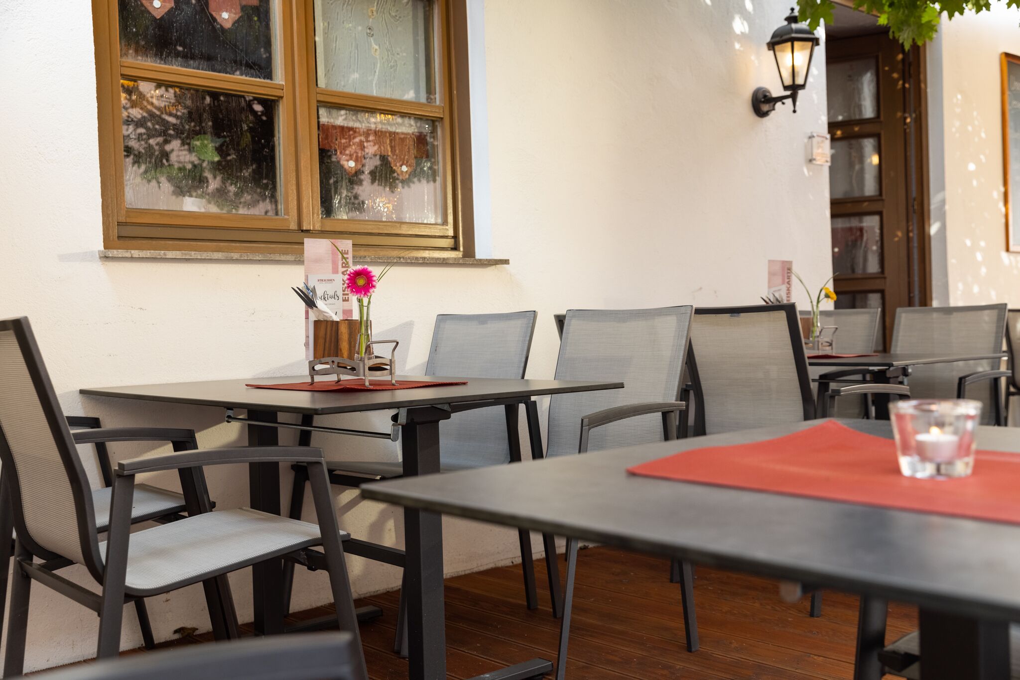An outdoor dining area with tables and chairs, a window with a view, and a wall-mounted light fixture.