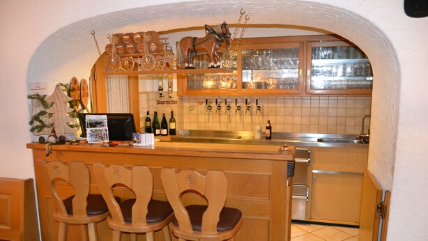 Uma cozinha com banquetas de madeira, um espaço para vinhos e um cabideiro suspenso.