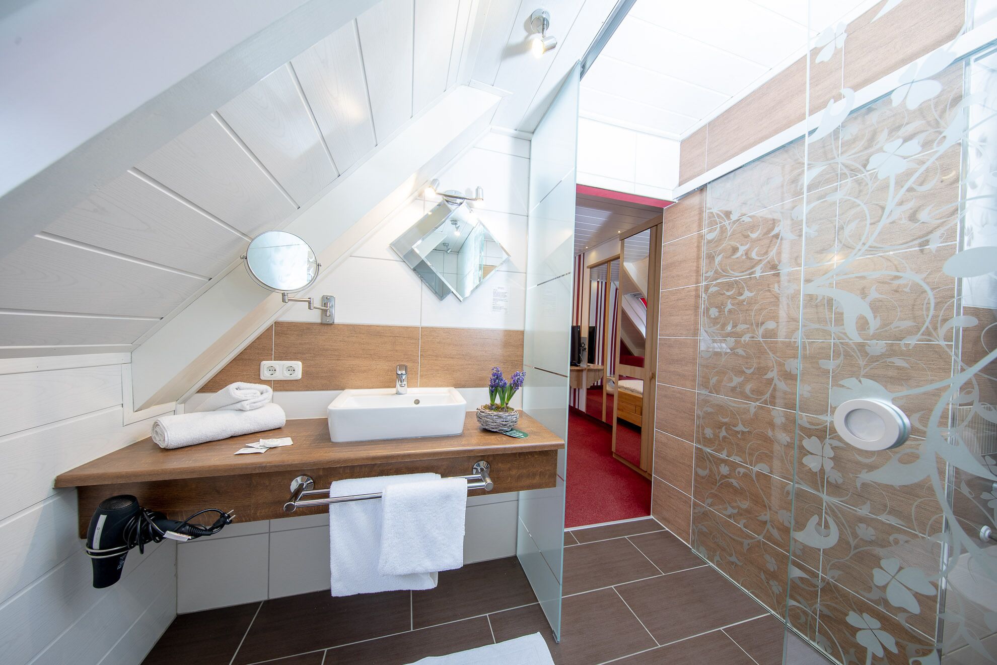Une salle de bain moderne avec un meuble-lavabo en bois, un miroir, un lavabo et un espace douche agrémenté de carreaux à motifs.