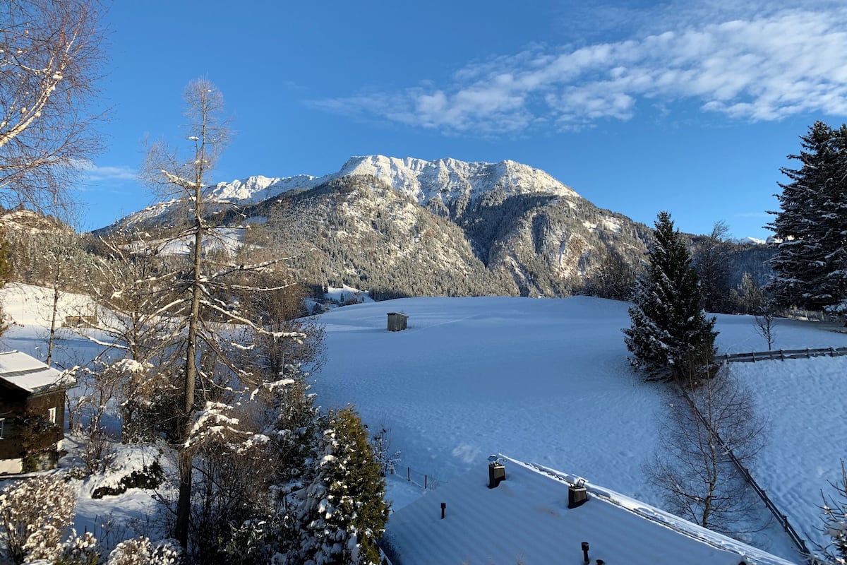 Een besneeuwd landschap met een berg op de achtergrond, een houten chalet en een skilift.