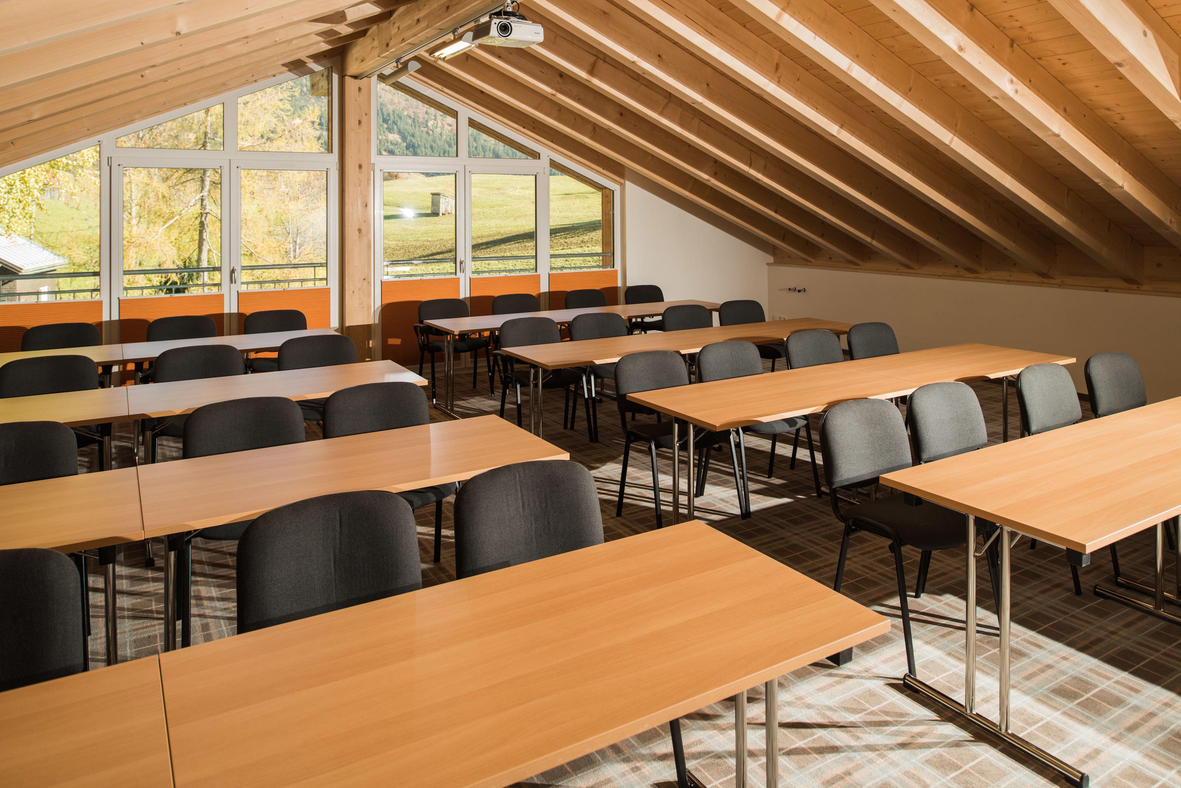 A conference room with multiple tables and chairs, large windows with a view of a green landscape, and a wooden ceiling.