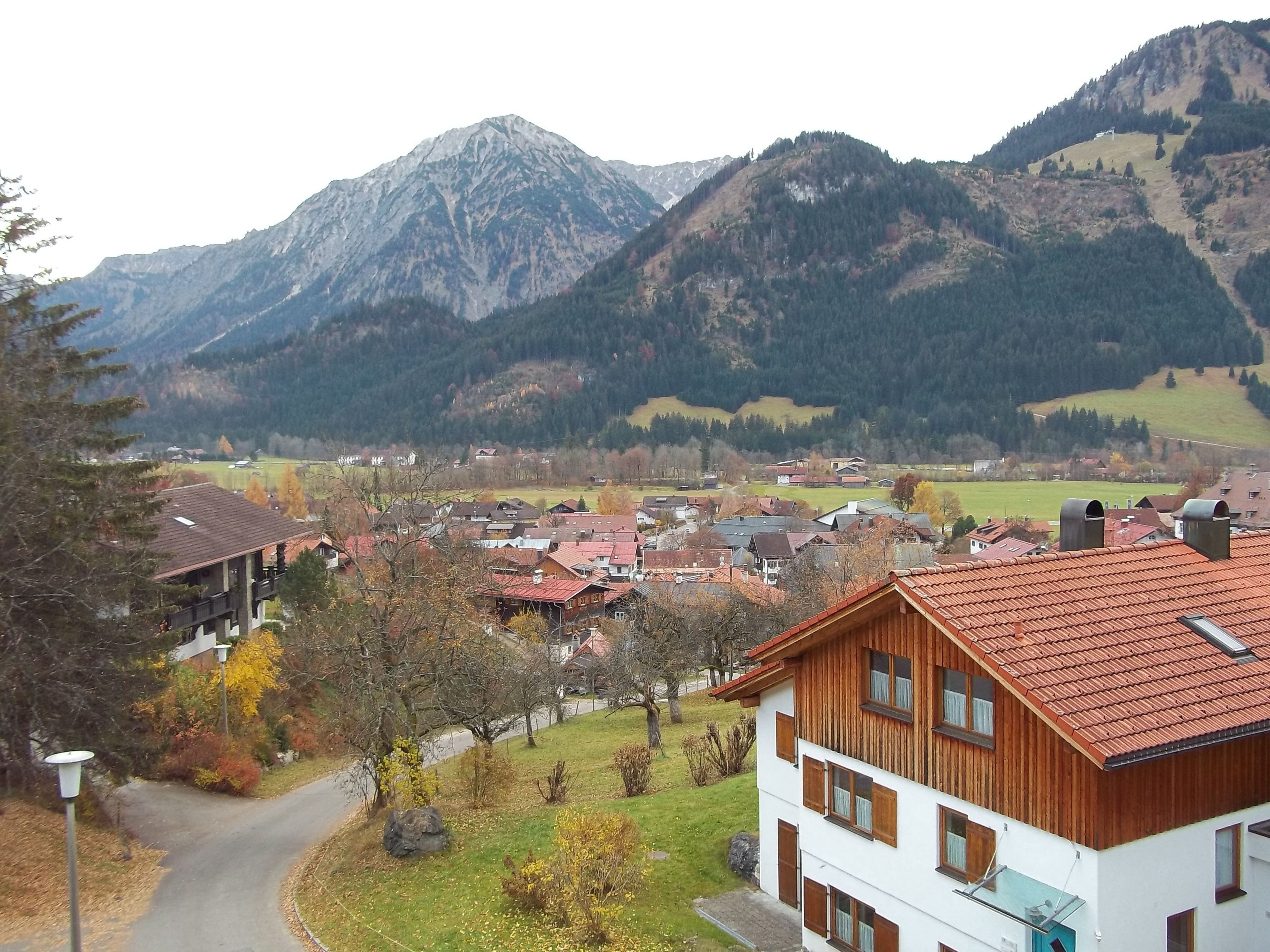Un pueblo de montaña con casas de madera tradicionales, un camino sinuoso y vistas de las montañas circundantes.