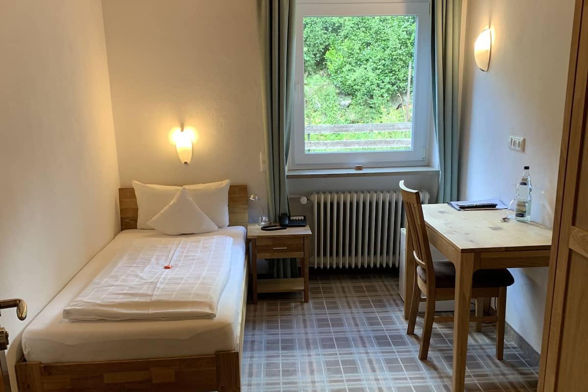 Een hotelkamer met een bed, bureau, stoel, raam met gordijnen en een radiator.