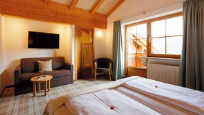 Ein Hotelzimmer mit Bett, Sofa, Sessel, Fernseher und einem Fenster mit Vorhängen.