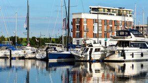 Un port de plaisance où sont amarrés de nombreux bateaux, un immeuble doté de balcons et un ciel dégagé.