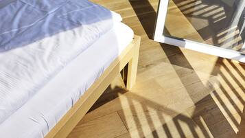 Een houten bed met wit beddengoed in een kamer met houten vloeren en een groot raam.