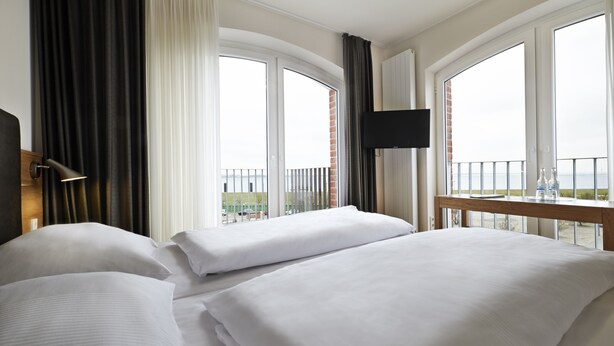 Une chambre d’hôtel avec deux lits, une télévision et de grandes fenêtres donnant sur la mer.