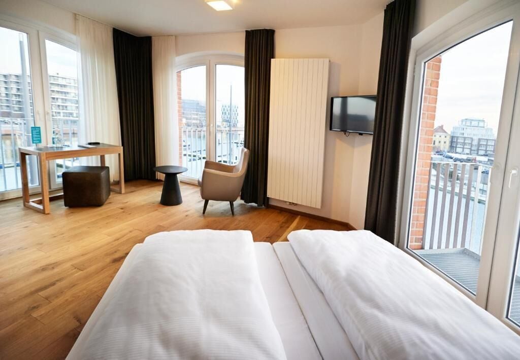 Habitación de hotel con cama, escritorio, silla, televisor y balcón con vistas a la ciudad.